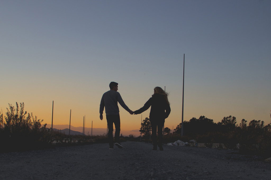 Eine Frau und ein Mann gehen Hände haltend Richtung Sonnenuntergang