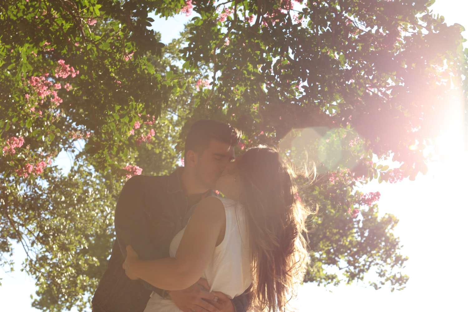 Küssendes Paar unter blühendem Baum im Sonnenlicht