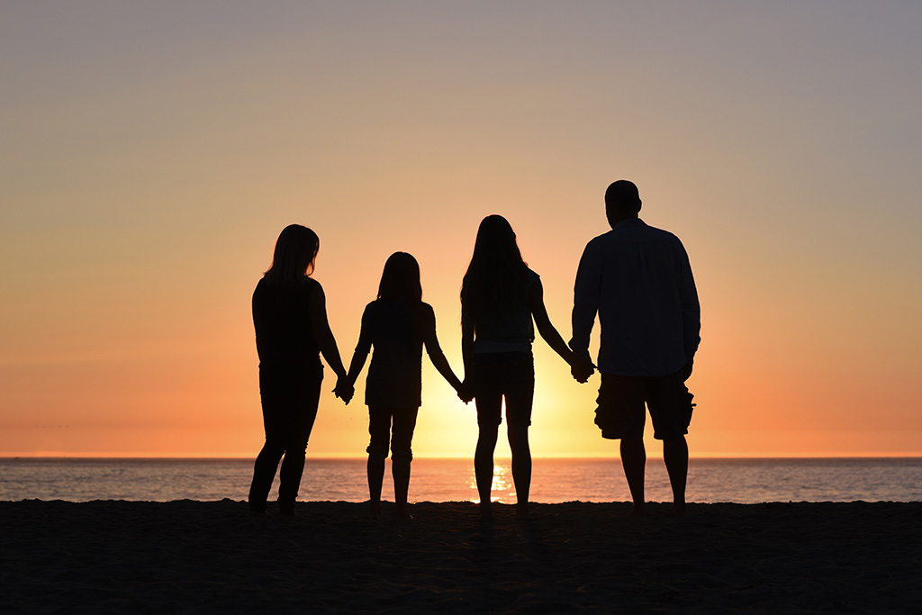 Silhouette einer Familie vor Sonnenuntergang an Strand stehend