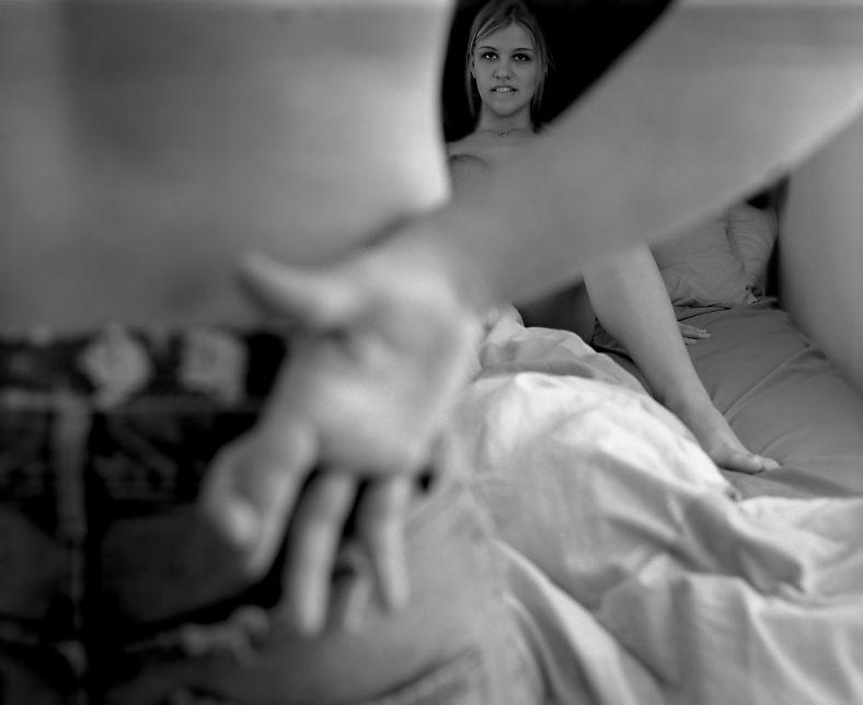 Frau sitzt lustvoll im Bett, ihr Partner kreuzt auf sie zukommend die Finger