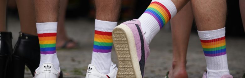 diverse Beine mit Turnschuhen, weißen Socken und Pride Flag Ringeln